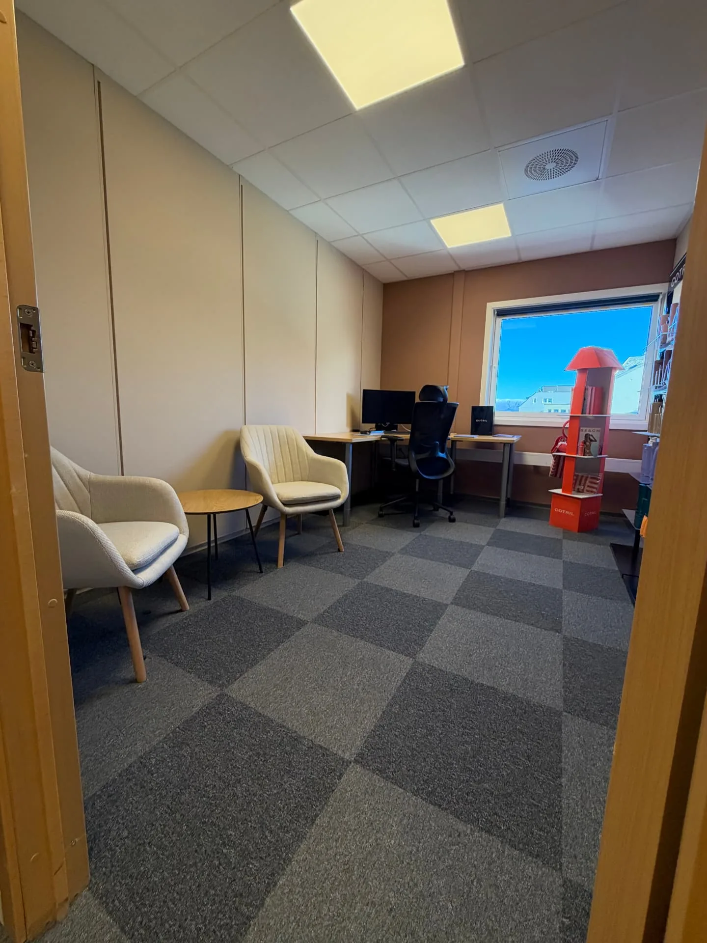 Lukket kontor hos VÆXT, sett gjennom ei åpen dør med skrivebord, monitor, kontorstol og to gjestestoler.